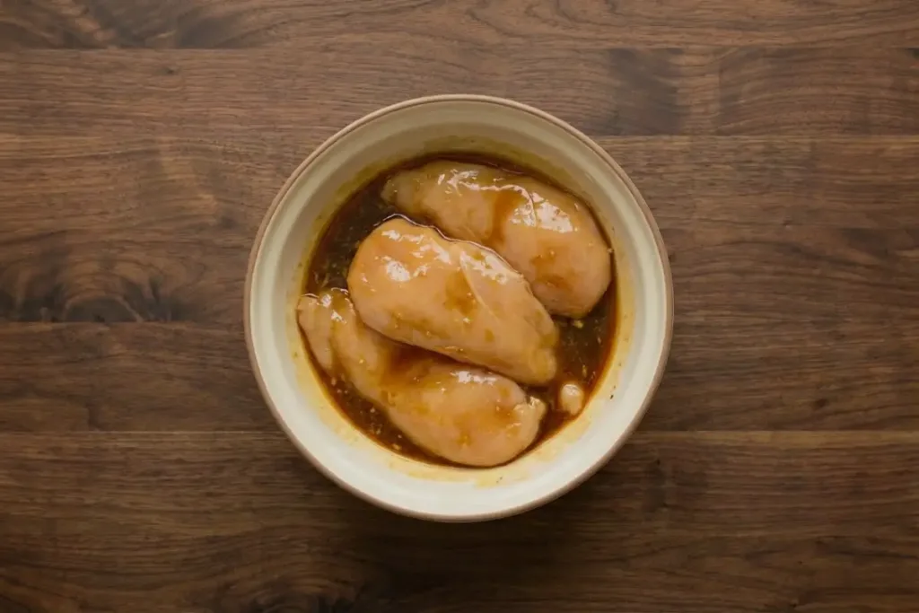 Air Fryer Maple Chicken Breast — Sticky-Sweet, Juicy, Fast Air Fryer Maple Chicken Breast Raw chicken breasts soaking in marinade inside a bowl on a dark wooden surface